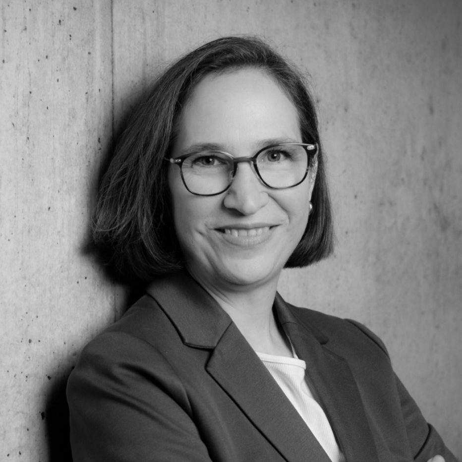 Petra Ringmann trägt einen grauen Blazer vor einer Betonwand.