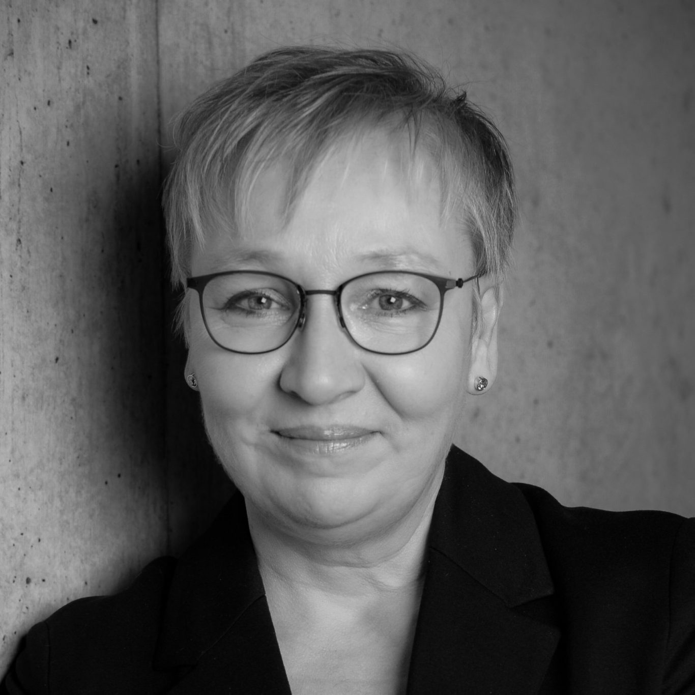 Porträt von Iris Bothe lächelnd mit kurzen blonden Haaren und Brille, im schwarz-weißen Stil.